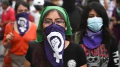 Kobieta w zielonej chuście na głowie i fioletowej chuście zasłaniającej usta, otoczona innymi kobietami podczas protestu w Limie w Peru.