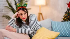 Сумна молода жінка сидить на дивані вдома під час різдвяних свят