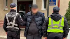 Двоє поліцейських тримають чоловіка за руки. У нього заблюрене лице 