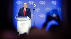 Donald Trump discursando no pódio do Fórum Econômico Mundial em Davos, Suíça, em 21 de janeiro de 2026. À direita da imagem, alguém segura um telefone acima da cabeça e tira uma foto com ele.
