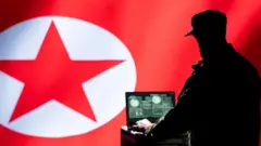 شخص يعمل على جهاز لابتوب وفي الخلفية علم كوريا الشمالية 