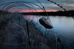 Calçado pendurado em cerca de arame farpado ao longo de um rio