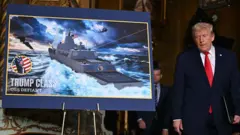 新しい「トランプ級」戦艦の画像の横に立つトランプ氏。 