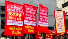 মঙ্গলবার সকালে এরকম প্লাকার্ড নিয়ে নিম্নতম মজুরি বোর্ডের কার্যালয়ের সামনে দাঁড়ান পোশাক শ্রমিকরা 
