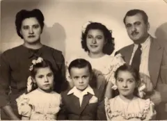 La madre de Alejandra Jáidar, con un vestido oscuro, está parada en la parte izquierda. A su lado y en el centro de la foto está Alejandra, de adolescente, con un vestido blanco y un adorno blanco en la cabeza. A su lado está su padre, vestido de traje y corbata. Delante de ellos están tres niños, uno de ellos es un niño que está en el centro