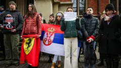 Estudantes seguram uma bandeira da Ferrari e uma bandeira da Sérvia em um protesto na Polônia, em solidariedade aos protestos na Sérvia.