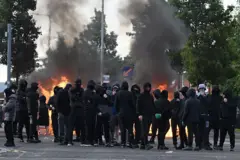 Jóvenes encapuchados con fuego detrás.