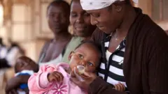 Мать дает ребенку противомалярийный препарат