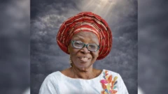 Mama Debirah Fasoyin wọ aṣọ funfun pẹlu gele ati igo loju rẹ