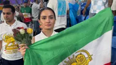 Uma jovem segura um buquê de rosas e uma bandeira iraniana verde, branca e vermelha com o sol e o leão
