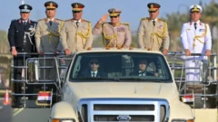 الرئيس السيسي يرتدي زياً عسكريا ويؤدي التحية العسكرية من على عربة عسكرية مكشوفة وبجواره قادة الجيش المصري في افتتاح مبنى الأوكتاغون