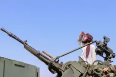 یک نیروی طالبان که بالای یک وسیله ثقیله نظامی قرار دارد به آسمان نگاه می‌کند