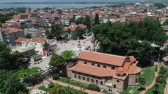 Vista aérea da Mesquita de Santa Sofia Orhan, um ornamentado edifício de tijolos com pequenas cúpulas e um único minarete, em frente a uma pequena praça e rodeado de jardins bem cuidados. Ao fundo, pode-se ver o lago, no outro lado da cidade.