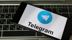 Колаж, на якому смартфон із заставкою телеграма лежить на темній клавіатурі ноутбука.