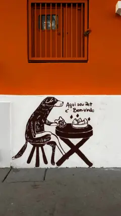 Pintura feita à mão na parede de bar em Porto Alegre, Rio Grande do Sul, mostra um cachorro de pernas cruzadas sentado em uma mesa de bar servida com um osso, uma bebida e uma porção de coxinhas. Acima se lê: "Aqui seu pet é bem-vindo"