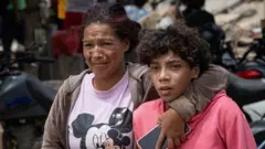 Una mujer y un niño juntos frente a escombros en venezuela. la mujer llora. 
