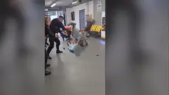 پلیس منچستر به سر متهمی که در فرودگاه روی زمین افتاده بود با لگد کوبید