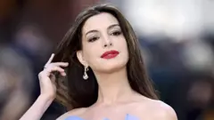 A atriz Anne Hathaway, com a mão direita nos cabelos