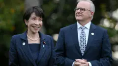 紺のセットアップに真珠のネックレスを着けた高市氏と、ダークスーツを着たアルバニージー氏が並んでいる