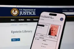Vista de la ficha policial de Epstein en un teléfono y detrás un monitor que muestra la página web del Departamento de Justicia de EE.UU.