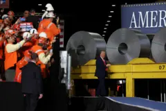 Trump caminhando em palco repleto de rolos de aço, aparentemente