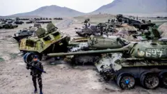 لاشه‌های تانک‌ها و سرباز مسلح روس در کنارشان ایستاده است