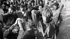 Foto em preto e branco mostra homens capturados infileirados com as mãos na cabeça