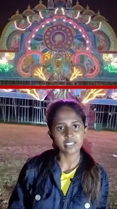 විදුලි බුබුළු දල්වා ඇති තොරණයක් ඉදිරිපිට තරුණියක් සිටී.