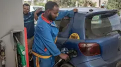 የነዳጅ ማደያ ሠራተኛ ወደ መኪና ነዳጅ እየቀዳ