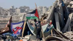 پسربچه‌ای در حال نصب پرچم فلسطین را در میان ویرانه‌ها در خان یونس در جنوب غزه 