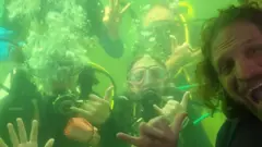 Dituri dentro do alojamento submerso enquanto um grupo de mergulhadores posa para foto com ele do lado de fora