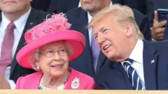 A rainha Elizabeth 2ª, usando chapéu rosa e casaco combinando, está sentada ao lado de Trump, que se inclina, presumivelmente em conversa. Ele veste terno azul-marinho com um pequeno broche da bandeira americana na lapela.