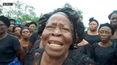 Ụfọdụ ụmụnwaanyị Uzzi ji akwa na bata ogige ụlọikpe ukwu Ụmụahịa maka okwu ala ha.