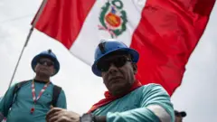 Dois operários com capacetes e uma bandeira do Peru tremulando ao fundo