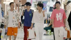 Cuatro hombres caminando con bolsas por un centro comercial