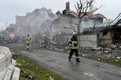 Casas destruídas por bombardeios em Kiev. Duas pessoas do Corpo de Bombeiros caminham pela rua