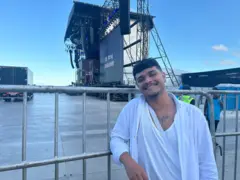 Homem apoiado em gradil, com palco ao fundo