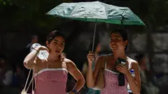 Dve mlade žene nose flaše vode i telefone sklonile su se od vrućine pod kišobranom