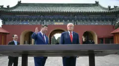 Os presidentes Xi e Trump se encontram no pátio de um complexo templário, atrás de uma grande exposição, com Xi levantando a mão para mostrar algo a Trump.