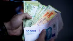 Um entregador da Pedidos Ya exibe os pesos argentinos ganhos durante uma entrega de comida em Buenos Aires, Argentina, em, 16 de dezembro de 2024