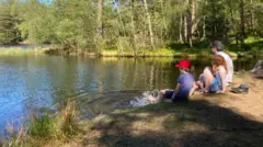 Patrick sitting and looking out across the Lake District with his children, who have their toes dipped in the water