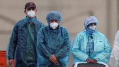 防護服を着けマスクをした人たちが歩いている