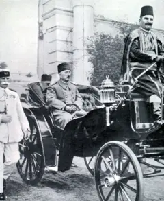 Mehmed VI, lleva un abrigo, está sentado en carruaje que transita por la calle. A su lado, camina un funcionario vestido de blanco
