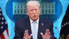 ダークスーツ姿のトランプ氏がホワイトハウスの記者会見場でマイクを前に立ち、両手を前に突き出して口を開いている