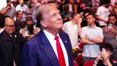 Trump olhando para o lado e sorrindo, observado por pessoas que tiram foto dele