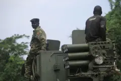 Abasirikare babiri ba Uganda bari hejuru y’imbunda ya rutura. Umwe muri bo yambaye impuzankano ya gisirikare, mu gihe undi yambaye umupira w’amaboko magufi w’igikara wanditseho amagambo “UPDF”.
