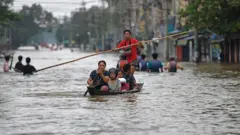 ၂၀၂၄ ခုနှစ်တုန်းက ပဲခူးမြို့က ရေကြီးမှု အခြေအနေဖြစ်ပါတယ်။ ပဲခူးမြို့လယ်မှာ ရေ လေးပေကျော်အထိ ရှိနေချိန် တီရှပ်အနီရောင်ဝတ် သက်လတ်ပိုင်း အမျိုးသားတစ်ဦးက သူအပါအဝင် လှေတစ်စီးပေါ် လိုက်ပါလာသူ ၅ ဦးကို ဝါးလုံးထိုးပြီး လှေလှော်နေပါတယ်။ လှေပေါ်မှာ လိုက်လာတဲ့ ရှေ့ဆုံးက အမျိုးသမီးကတော့ တုတ်တစ်ချောင်းကို လှော်တက်ပုံစံ လှော်ခတ်နေပါတယ်။ 