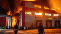 Двоє пожежних стоять біля палаючого будинку