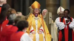 Sarah Mullally, con una túnica dorada, sonríe mientras varios obispos la aplauden.