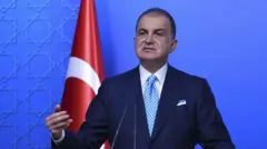 Ömer Çelik kürsüde konuşuyor. Arkasında Türk bayrağı var.
